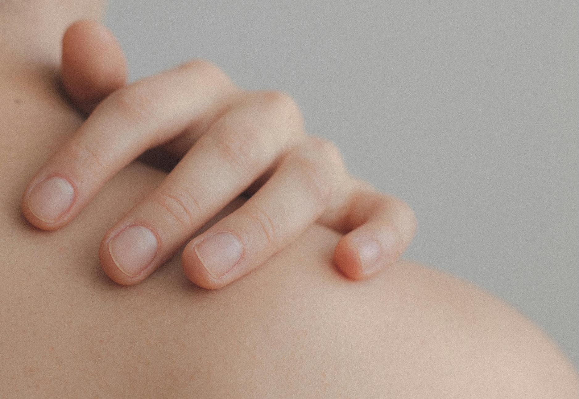 A close-up image of a person's hand gently resting on their shoulder. A close-up image of a person's hand gently resting on their shoulder.