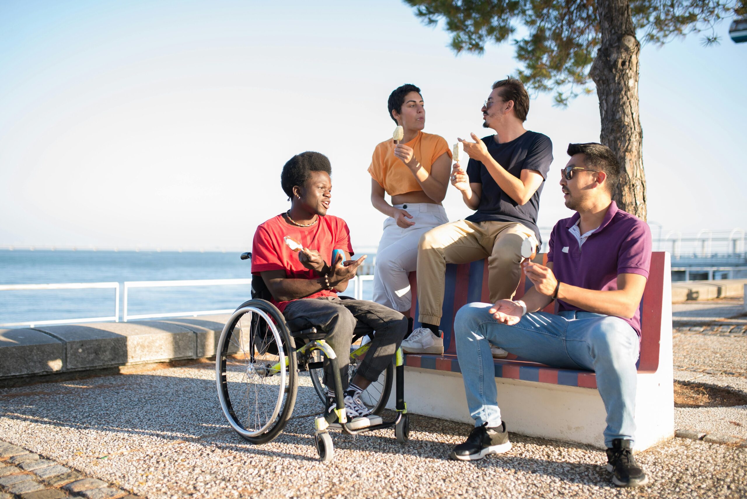 A group of young adults eating ice cream and having a conversation by the sea