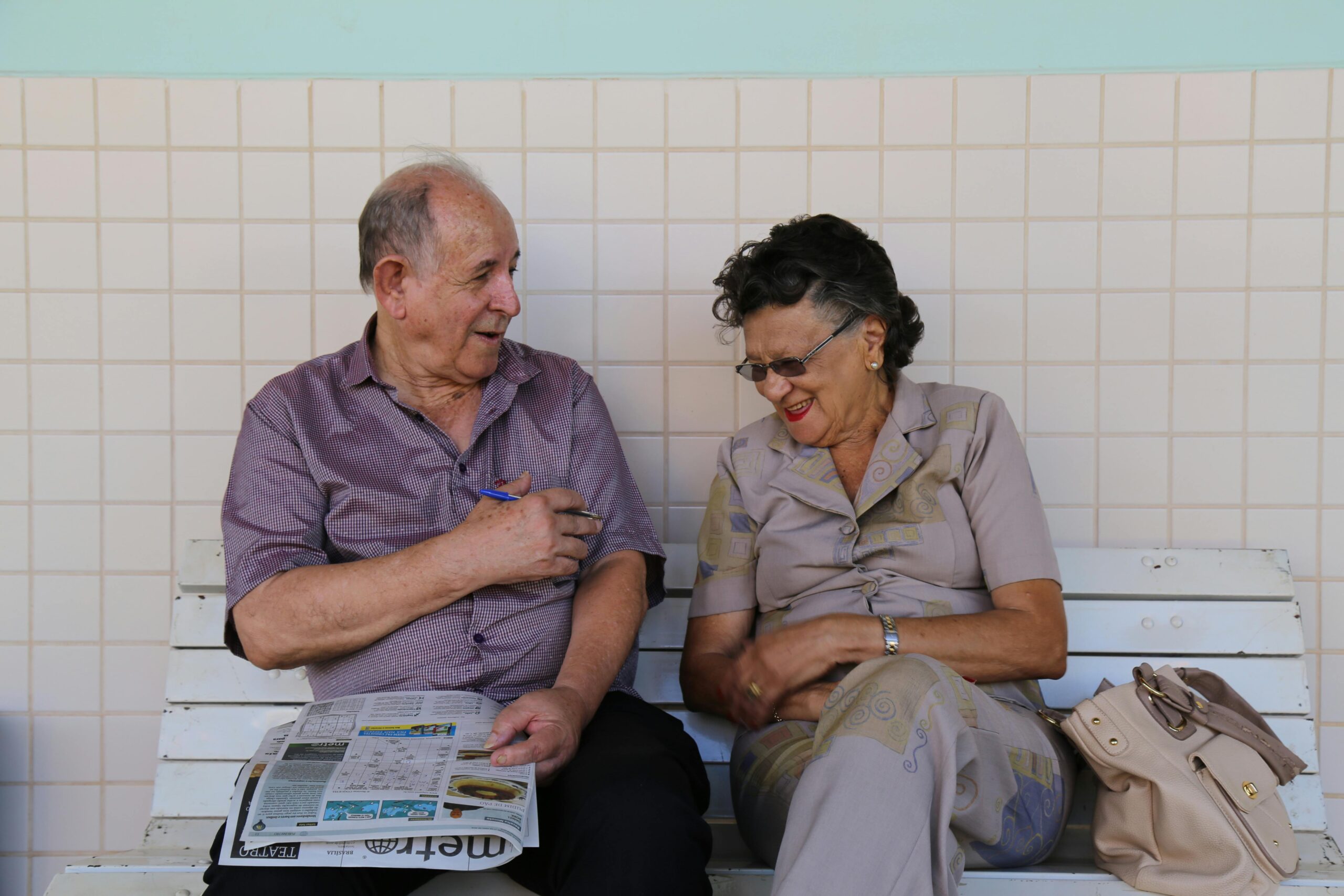 An elderly couple doing a crossword on a bench and laughing An elderly couple doing a crossword on a bench and laughing